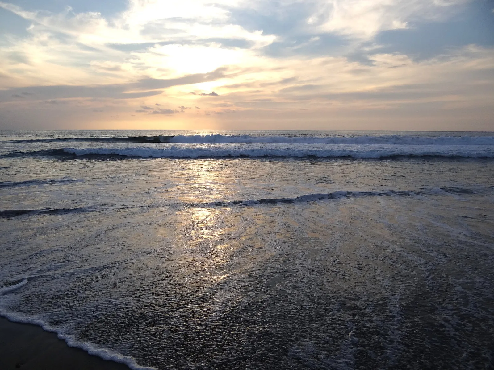 Atardecer en la playa de Zicatela, en Puerto Escondido: siluetas de surfistas y bañistas en la orilla con el sol bajo sobre el mar.