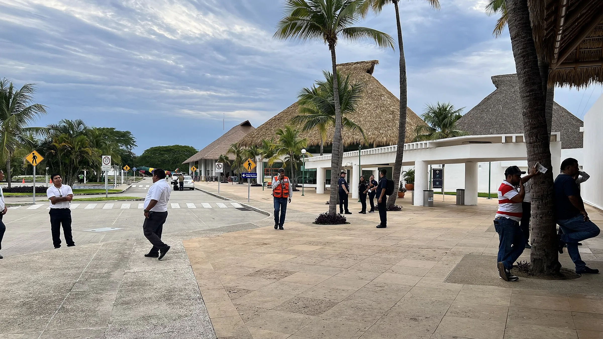 Acceso del aeropuerto de Huatulco: los techos de palapa sobre la terminal, palmeras altas alrededor y la acera de llegadas por delante.