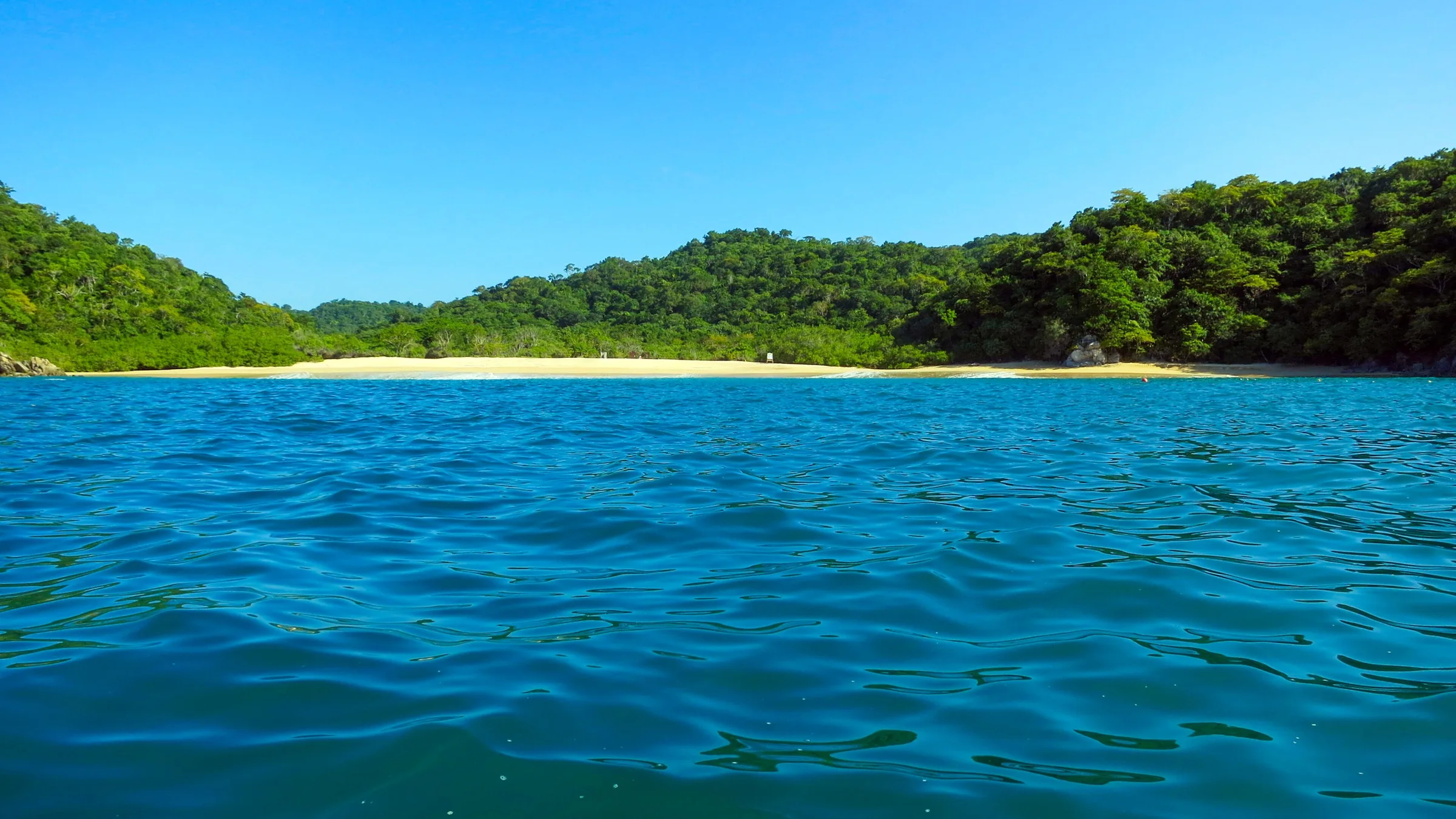 Una de las bahías vírgenes de Huatulco vista desde el agua: franja de arena clara cerrada por cerros de selva baja y, en primer plano, el Pacífico turquesa en calma.