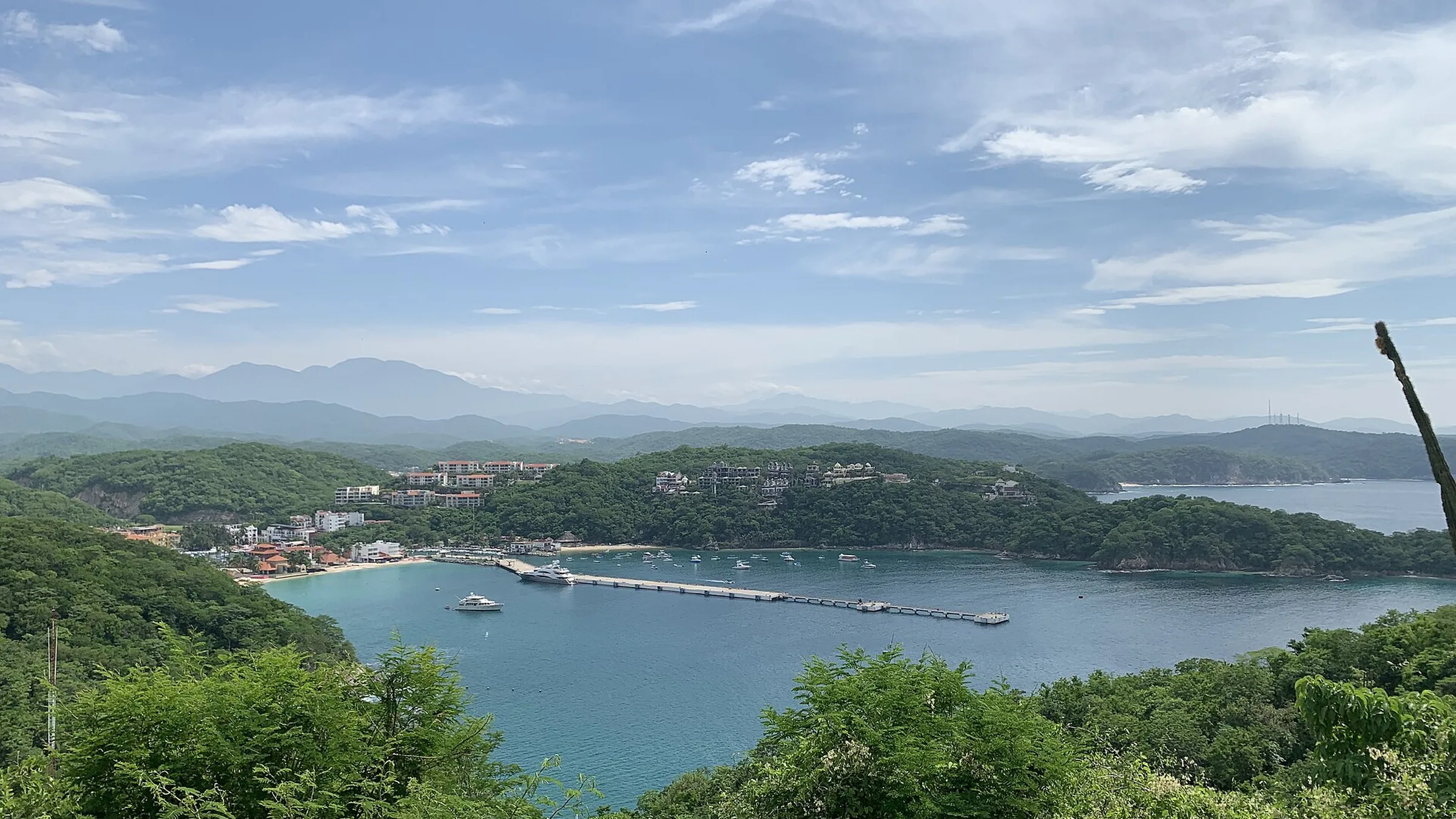 Vista de la bahía de Santa Cruz en Huatulco desde el mirador: el muelle de cruceros adentrándose en el agua turquesa, yates fondeados y los cerros verdes cerrando la bahía.
