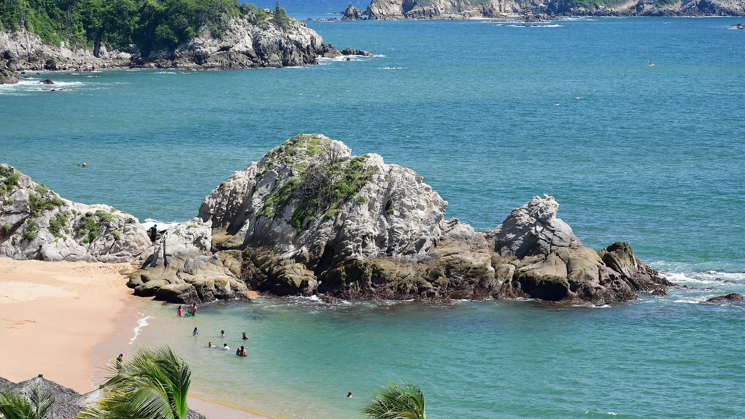 Bahía de Tangolunda, en Huatulco, con formaciones rocosas dentro del agua, arena clara y vegetación en el acantilado.